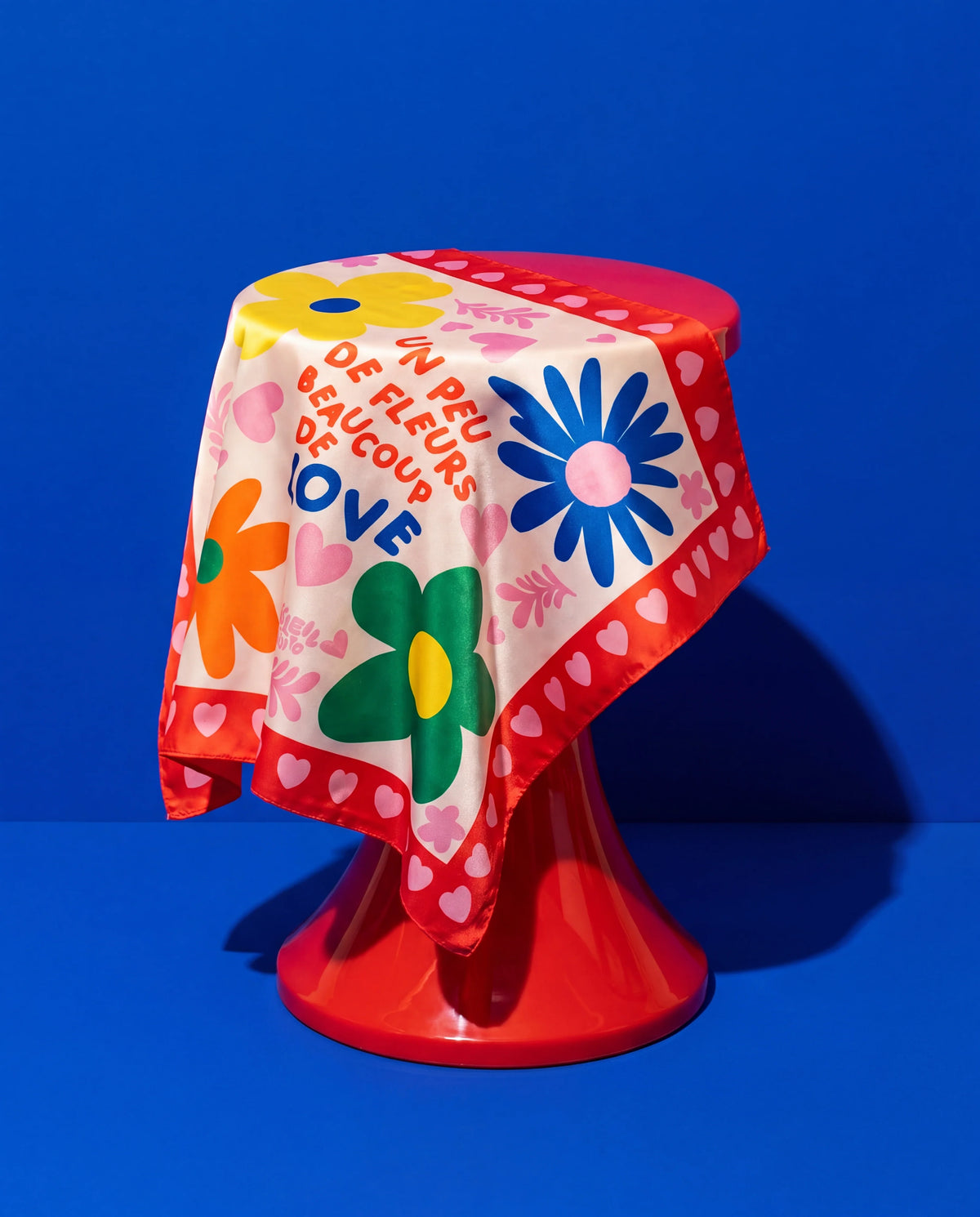 Foulard Fleurs & Love Soleil Mojito en satin coloré, motif fleurs et cœurs, drapé sur fond bleu