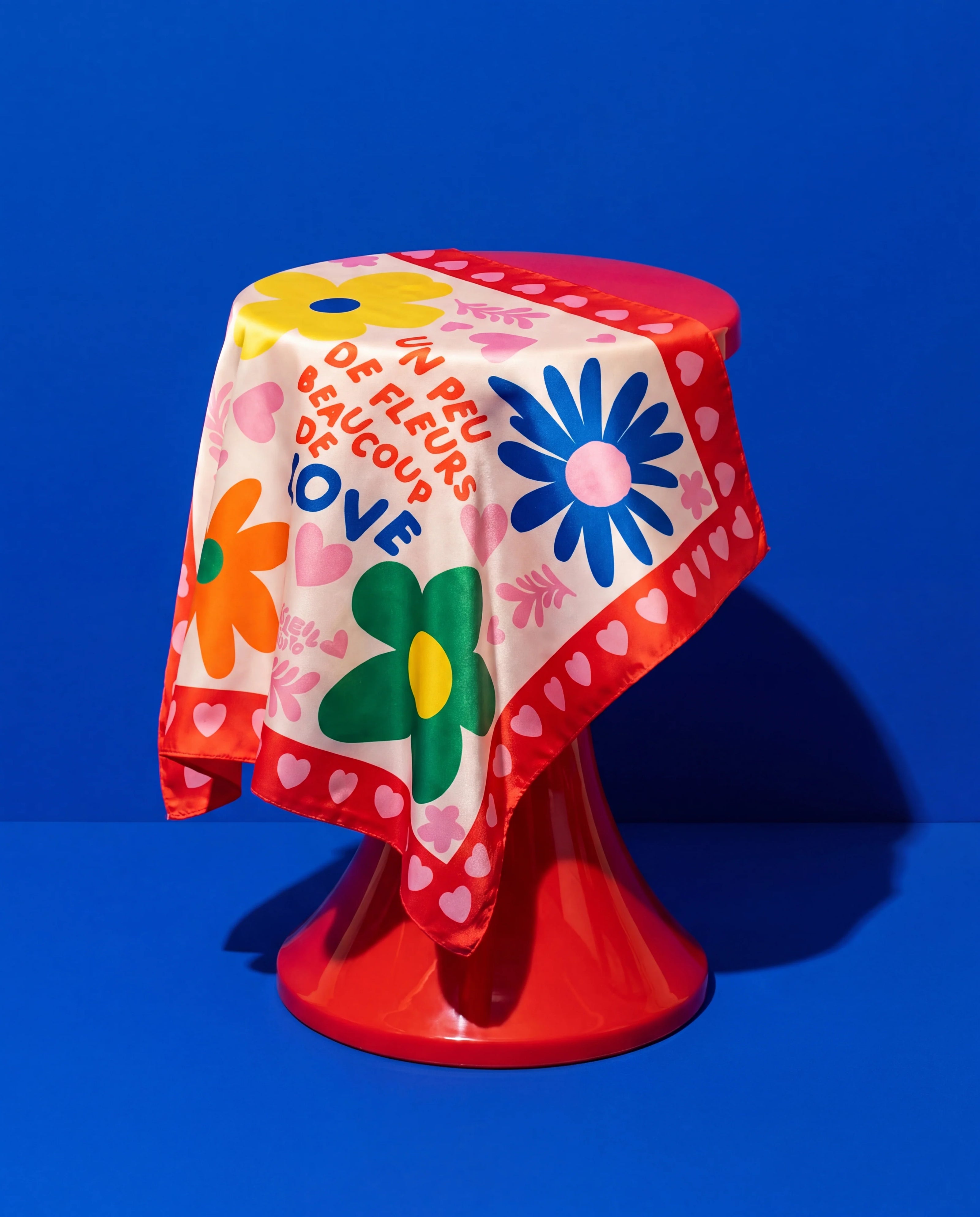 Foulard Fleurs & Love Soleil Mojito en satin coloré, motif fleurs et cœurs, drapé sur fond bleu