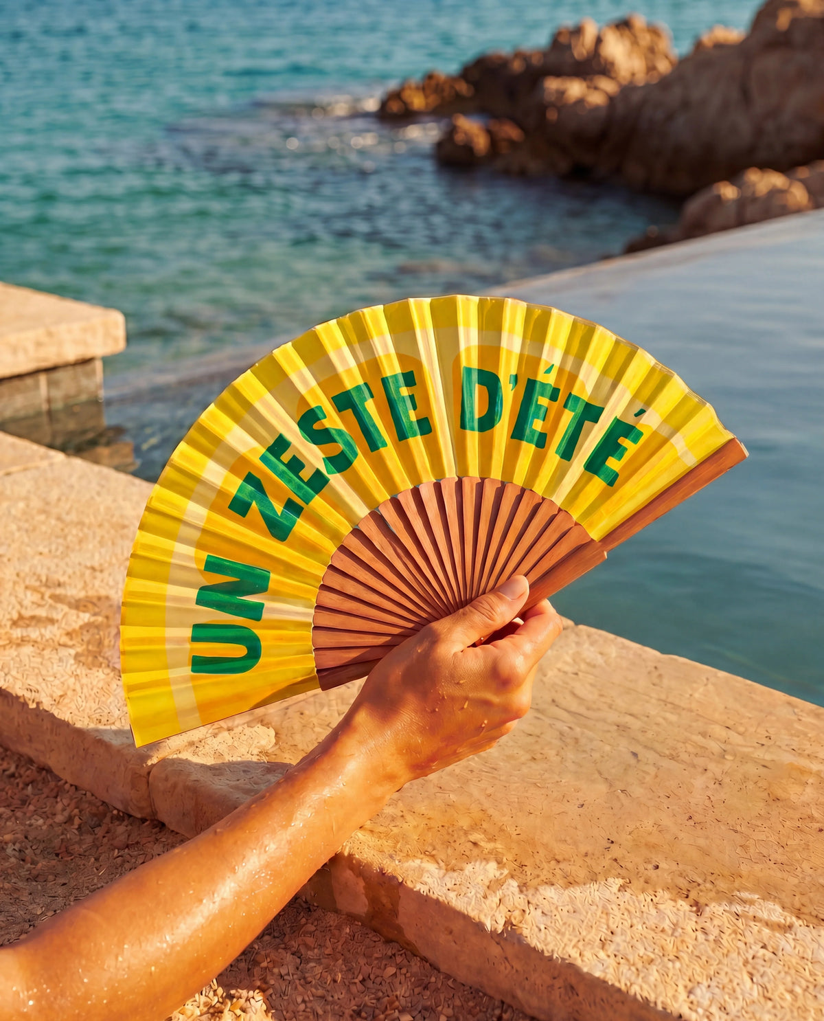 Éventail Zeste d'Été Soleil Mojito tenu en main près de la mer, accessoire d'été