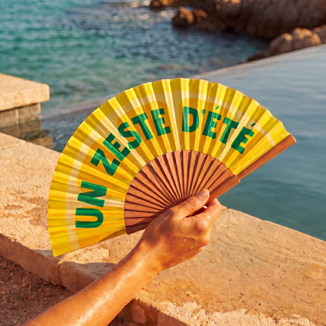 Éventail Zeste d'Été Soleil Mojito tenu en main près de la mer, accessoire d'été